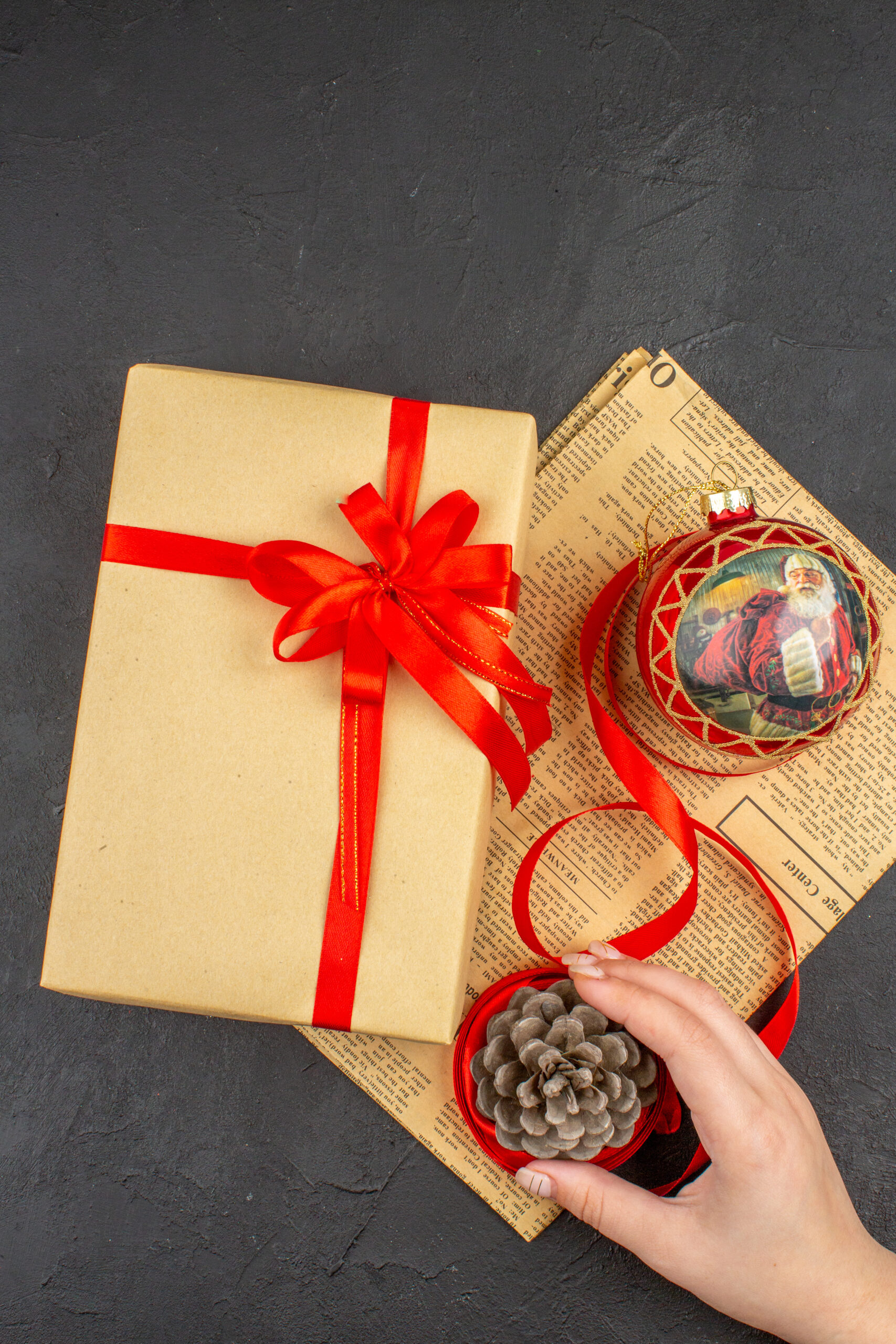 regalo-de-navidad-de-la-vista-superior-en-juguete-del-arbol-de-navidad-de-la-cinta-de-papel-marron-en-el-periodico-en-la-mano-femenina-en-la-superficie-oscura